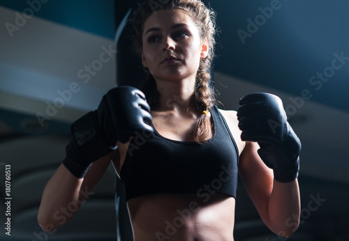 Young fighter boxer girl wearing boxing gloves before training. SHe is looking at opponent before match.