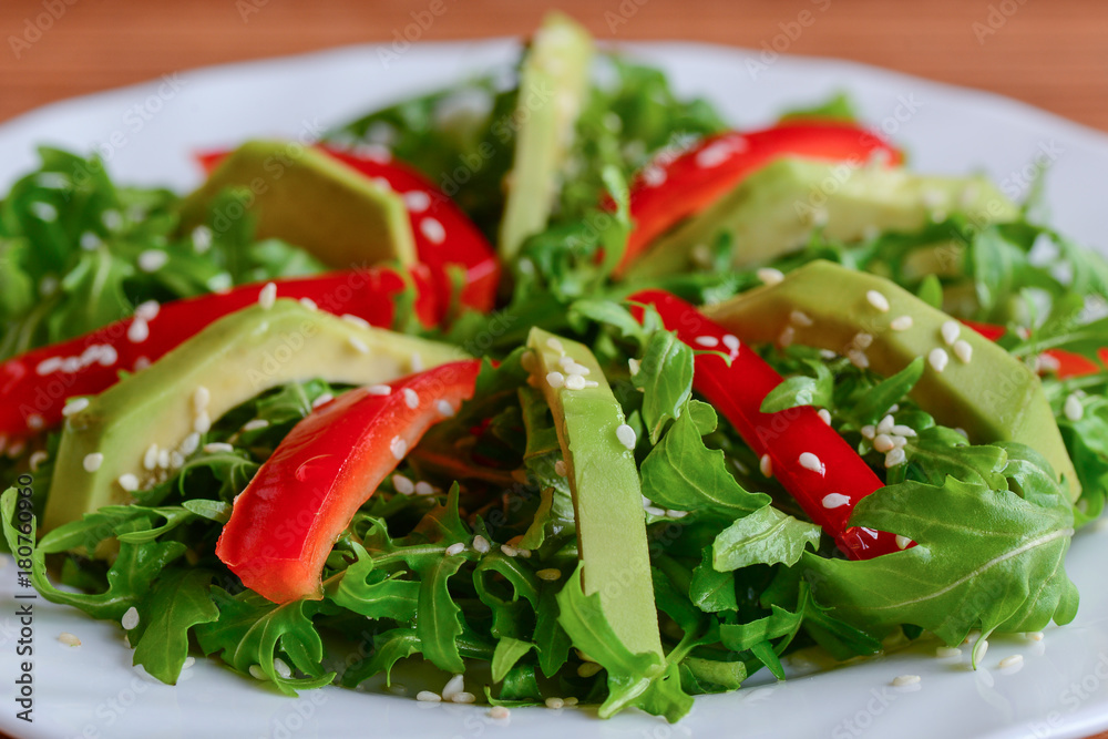Avocado, rocket and pepper salad. Simple rocket and avocado salad with fresh bell pepper and sesame seeds on a white plate. Healthy diet. Closeup Avocado, rocket and pepper salad. Simple rocket and avocado salad with fresh bell pepper and sesame seeds on a white plate. Healthy diet. Closeup