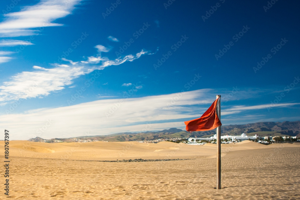 red flag on sand in desert with mountains and blue sky on background /red flag on the beach red flag on sand in desert with mountains and blue sky on background /red flag on the beach