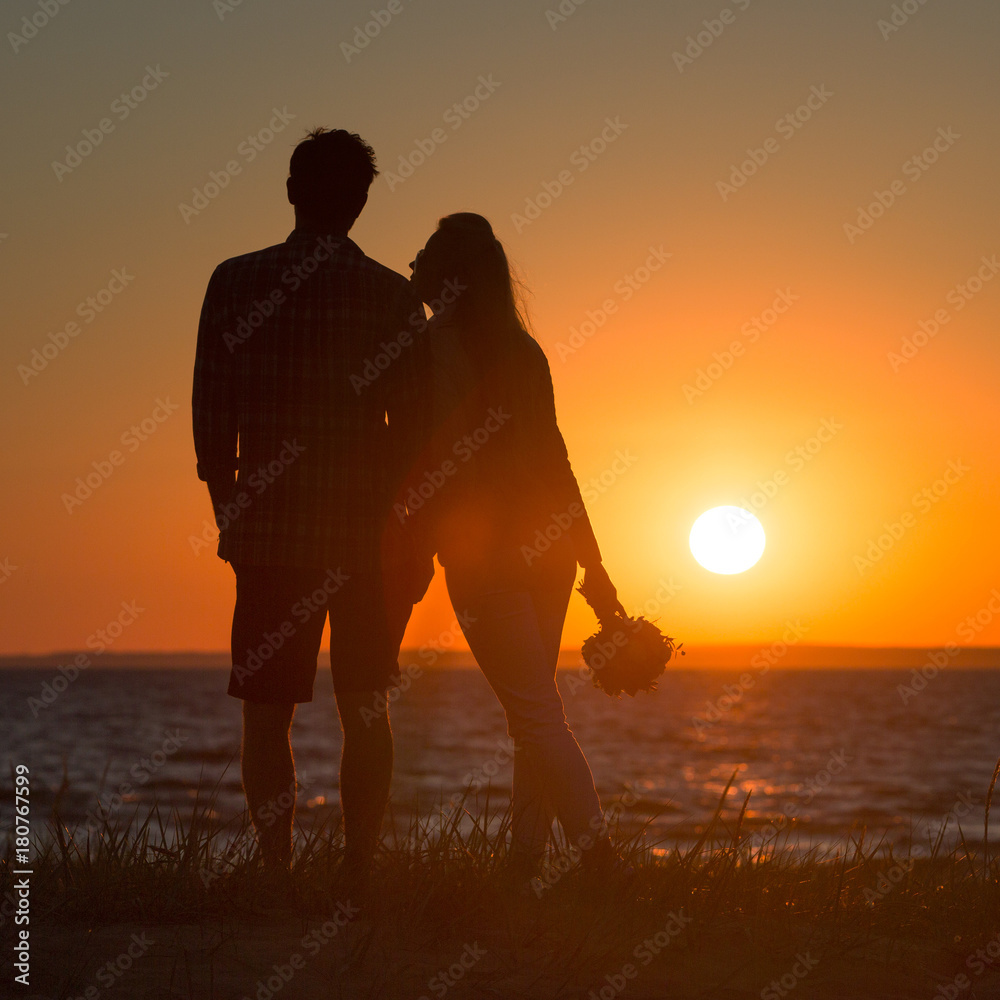 Couple on sunset/ Loving couple with bouquet standing on beach and looking at sunset