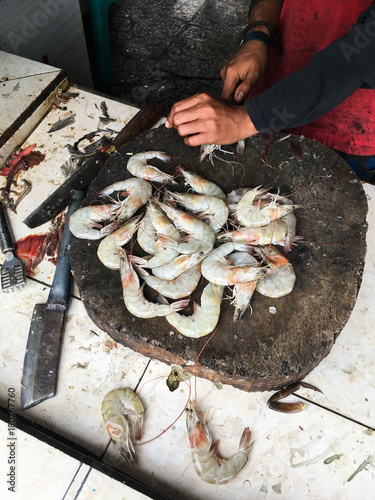 Hands in gloves of a man cleaning and cutting a shrimp on a table with many shimps aside/ fish market fish cleaning/ unsanitary conditions  photo