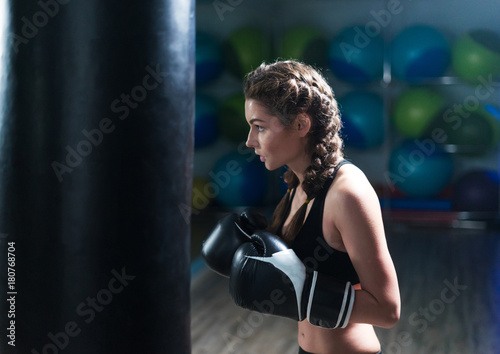 Young fighter boxer fit girl wearing boxing gloves in training with heavy punching bag in gym. Low key image. Woman power © Igor Kardasov