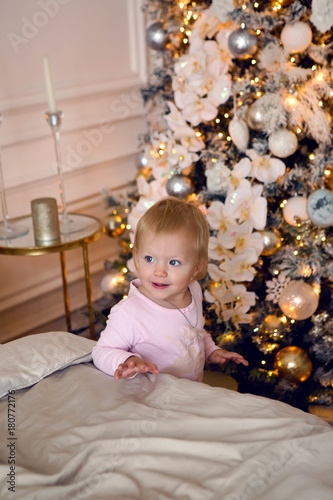 girl in pink pajamas having fun on a large bed on Christmas day with a Christmas tree