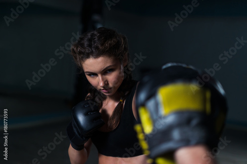 Young fighter boxer fit girl wearing boxing gloves in training  with  personal trainer in gym. Low key image. Woman power. She is focused on man's hand © Igor Kardasov