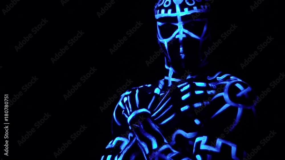 A black man in neon patterns stands with folded arms on his chest turns on the camera standing in a black room, slow motion A black man in neon patterns stands with folded arms on his chest turns on the camera standing in a black room, slow motion