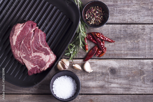 Ingredients for cooking healthy meat dinner. Raw uncooked beef steak on the iron grill pan with salt and pepper over wooden background. Top view. Copy space photo