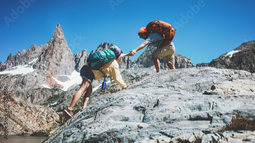 Young active couple with backpacks climbing rocks together in stunning snowy mountains. Natural wild near the lake