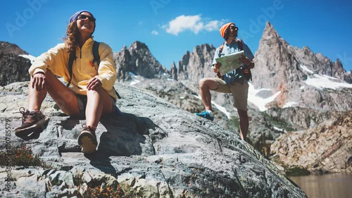 Obraz Młoda para aktywnych z plecakami wspinających się razem na skały w oszałamiającej górskiej dziczy. Odpoczywając i szukając nowych szlaków turystycznych na mapie