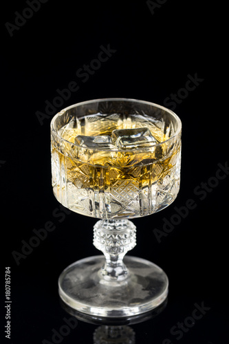 Crystal glass with yellow alcohol drink and ice cubes on a black background with reflections © zlajaphoto
