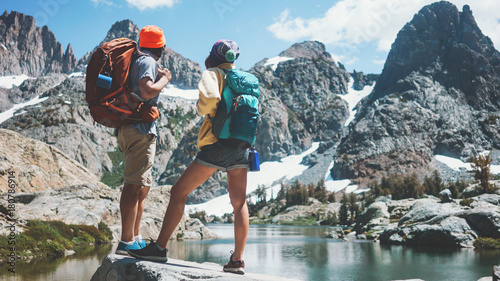 Young active backpackers couple rock climbing together in stunning mountain wilderness near the snowy lake. Looking at breathtaking natural landscape