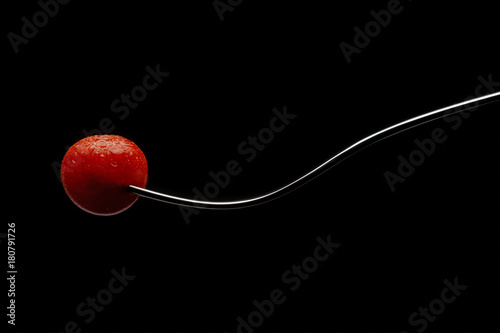 Wet cherry tomato on a fork with black background