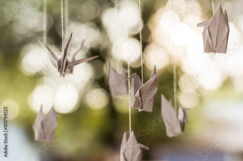 White folding paper birds hanging as mobile on natural blurry background