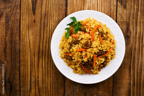 pilaf in a plate on wooden background, top view