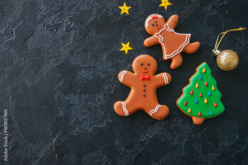 Festive Christmas background, Cookies with images of Gingerbread man and girl fir tree,  stars and ball on a black stone background. Top view with copy space.