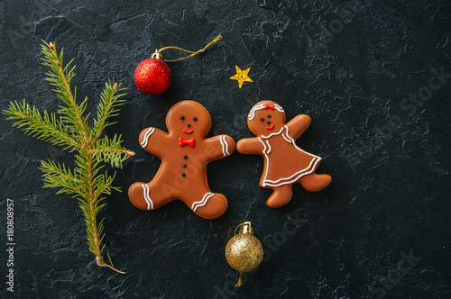 Christmas background. Gingerbread man and girl cookies, fir tree, balls on a black stone background. Top view.