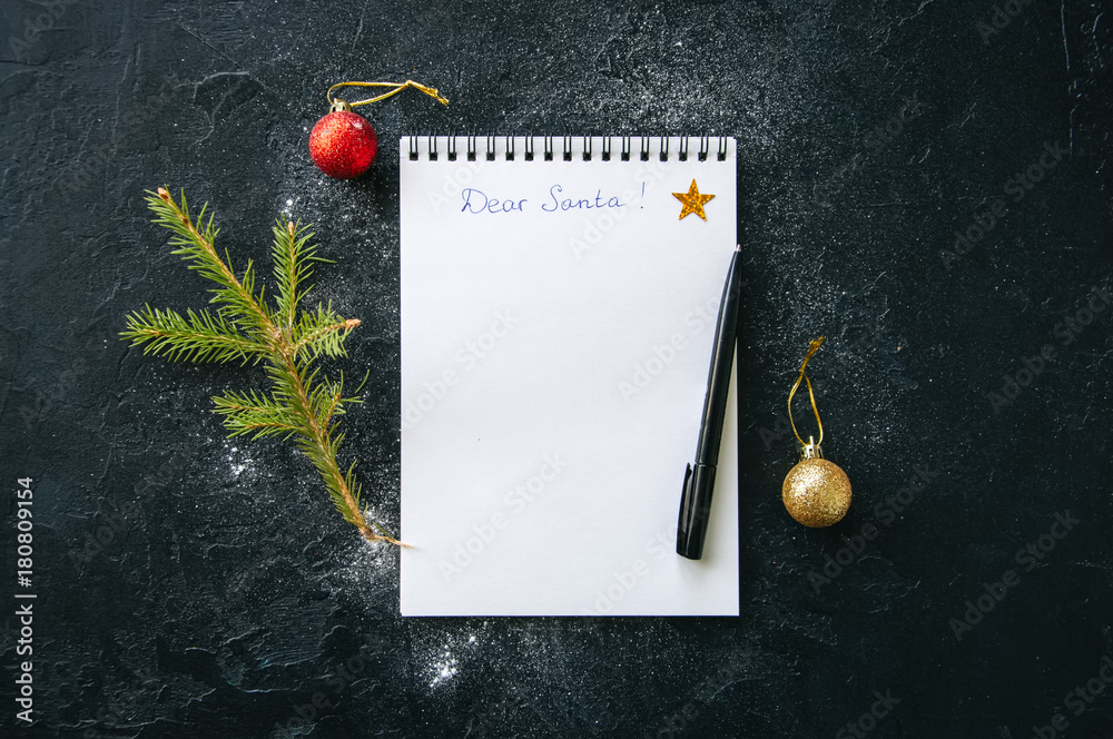 Φωτογραφία White page of notepad with inscription Dear Santa, fir tree branch, pen, balls on a black snowy background