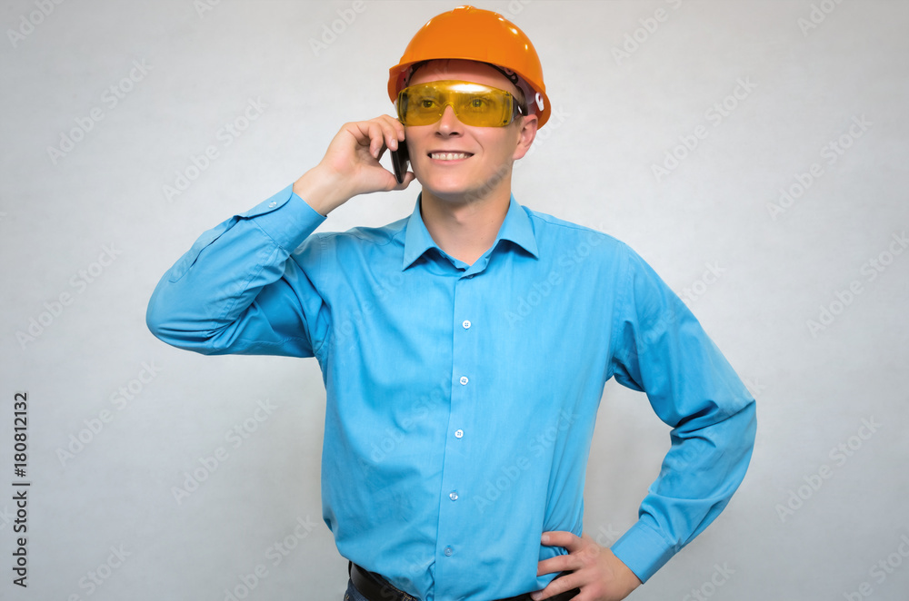 Young builder worker in hardhat helmet speaks by mobile phone isolated.