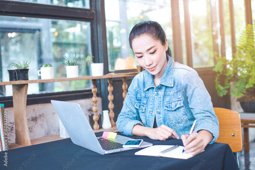 Woman works in a laptop computer and writing notepad with a pen in the office. Woman works in a laptop computer and writing notepad with a pen in the office.