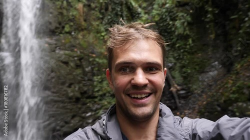 Happy man backpacker enjoying amazing tropical waterfall.Travel Lifestyle and success concept vacations into the wild nature on background mountain. 4k, slow motion photo