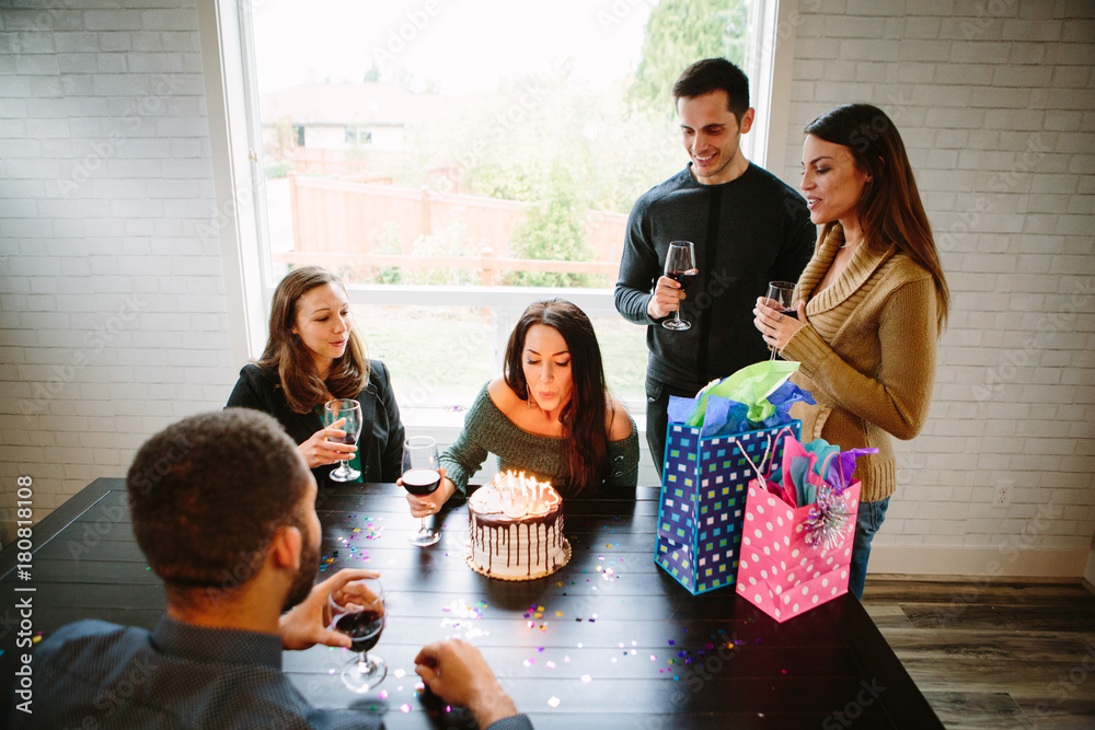 Obraz premium Woman blowing out candles on birthday cake with friends