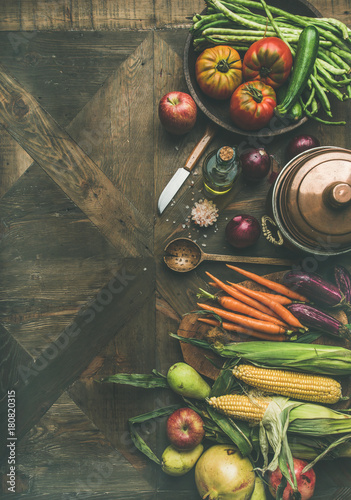 Fall cooking background. Autumn ingredients for Thanksgiving day dinner preparation. Flat-lay of green beans, corn cobs, carrot, tomatoes, eggplant, fruits over wooden table, top view, copy space