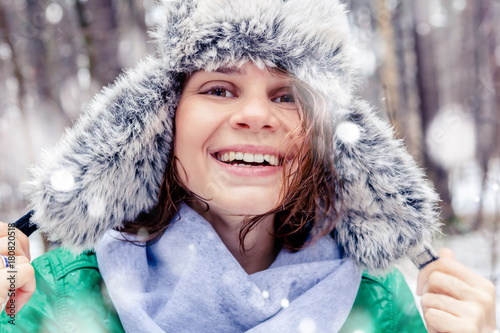 Portrait of a beautiful happy smiling young woman in a funny hat with a fur hat in a winter forest. Walks in winter