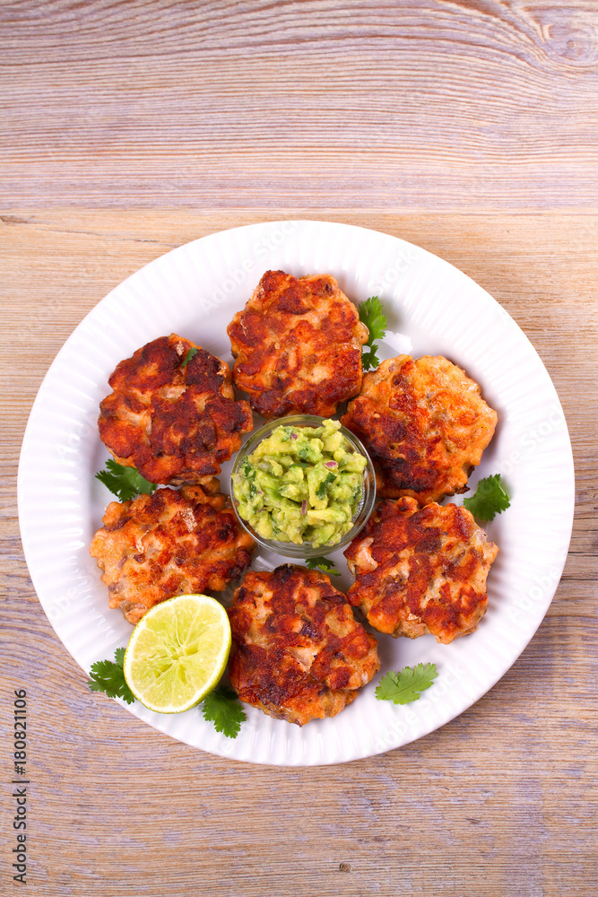 Salmon patties or cakes, lime and avocado on white plate. Fritters of fish. Salmon burgers. Healthy snack or take-away lunch bites, overhead Salmon patties or cakes, lime and avocado on white plate. Fritters of fish. Salmon burgers. Healthy snack or take-away lunch bites, overhead