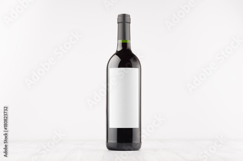 Dark wine bottle with blank white label on white wooden board, mock up. Template for advertising, design, branding identity.