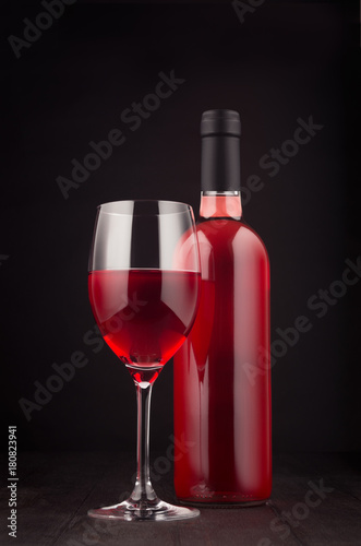 Bottle of rose wine and wine glass mock up on elegant dark black wooden background, vertical.