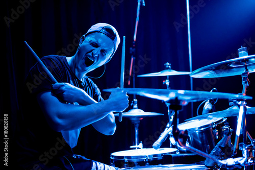 Fotografija Young drummer posing in front of the camera in a blue concert light