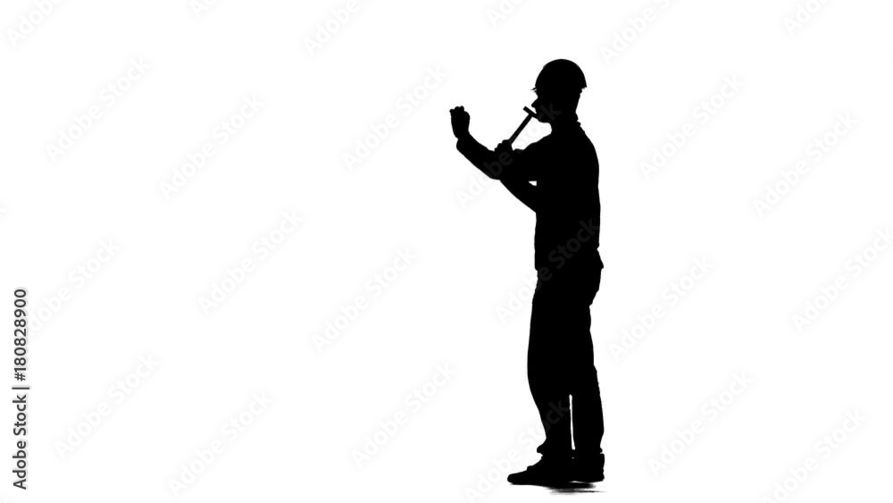 Worker in a helmet hammers a nail with a hammer. Silhouette. White background Worker in a helmet hammers a nail with a hammer. Silhouette. White background