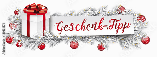 Heder mit einem Geschenkebox auf eingeschneiten Tannenzweigen mit Weihnachtskugeln mit Papierzettel und Text Geschenk-Tipp