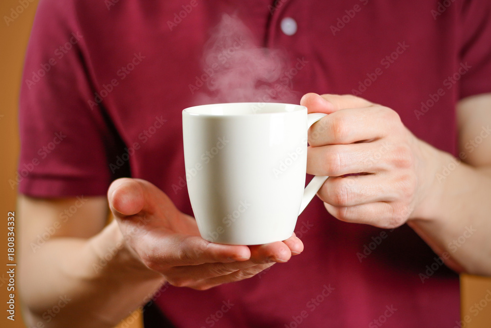 The man in the red shirt shows a clean white Cup. Cup for your design. Empty mug The man in the red shirt shows a clean white Cup. Cup for your design. Empty mug