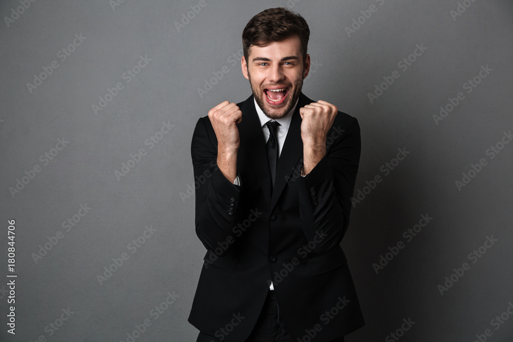 Close-up photo of happy attractive man in classic suit showing winner gesture, looking at camera Close-up photo of happy attractive man in classic suit showing winner gesture, looking at camera
