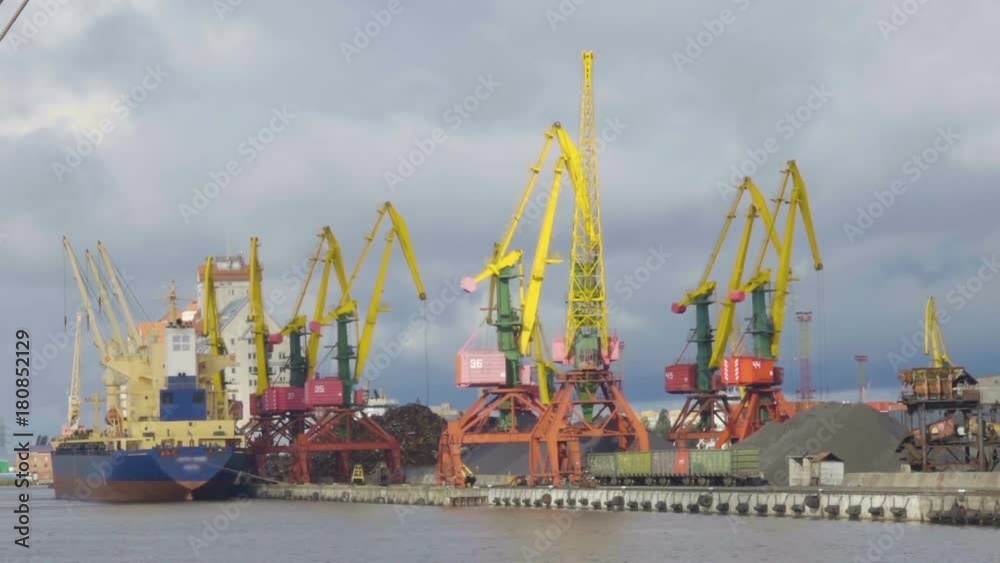 Cargo crane, freight train and coal in port. Cranes at the container port terminal. Scrap metal. Ship in the dock.