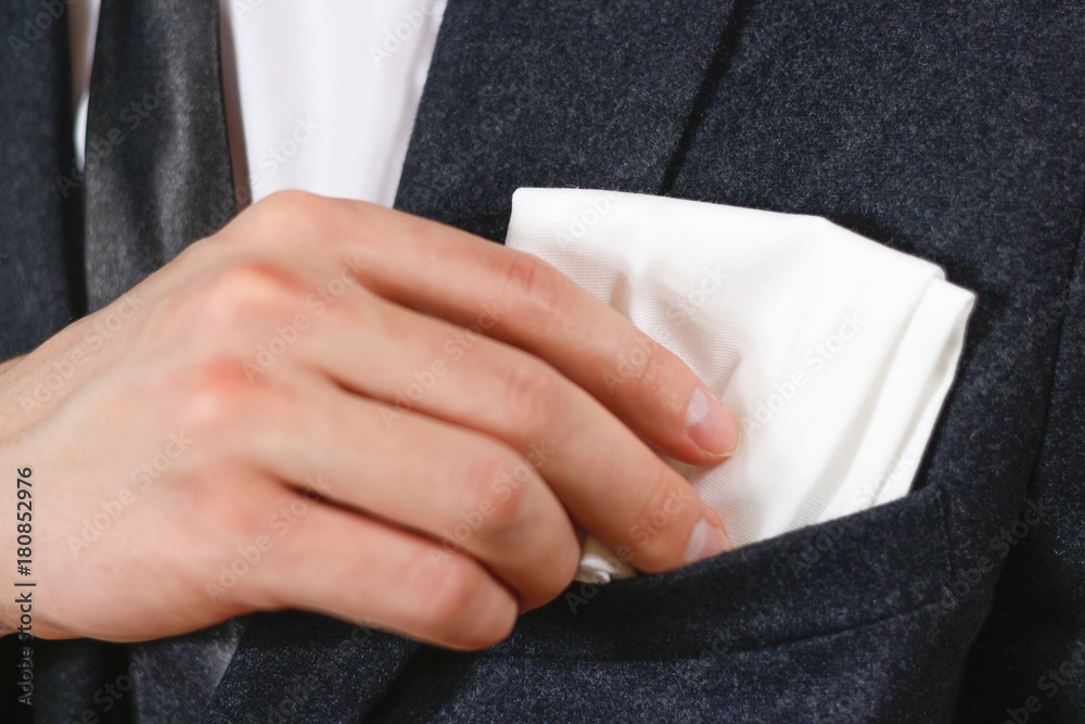 Close up hand puts a white handkerchief in the pocket of his black jacket