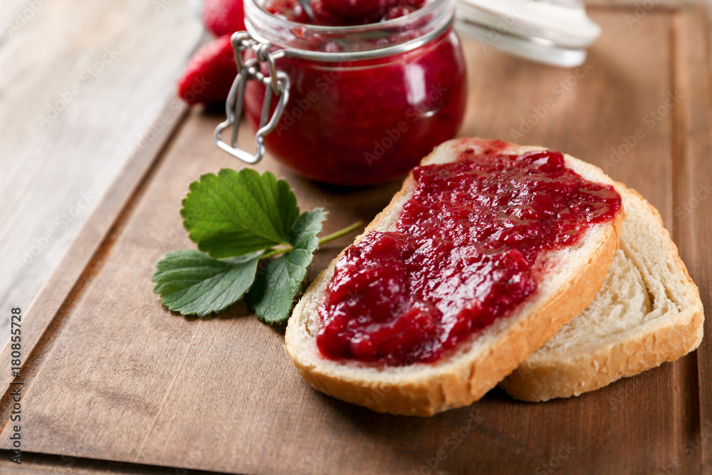 Bread and jar with strawberry jam on wooden board Bread and jar with strawberry jam on wooden board