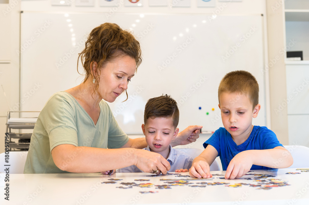 teacher woman and two preschooler boy playing with puzzle game in the classroom