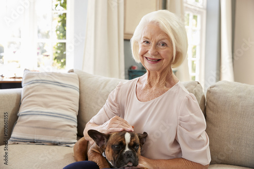 Senior Woman Sitting On Sofa At Home With Pet French Bulldog