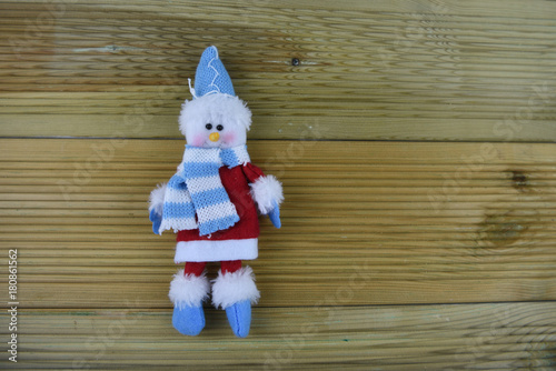 Christmas photography image with hand made knitted happy white snowman in blue hat scarf red coat and boots on natural wood background