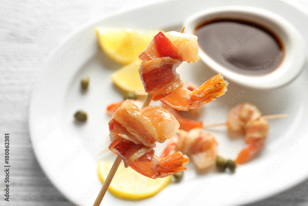 Bacon-wrapped shrimps on skewer over plate, closeup Bacon-wrapped shrimps on skewer over plate, closeup