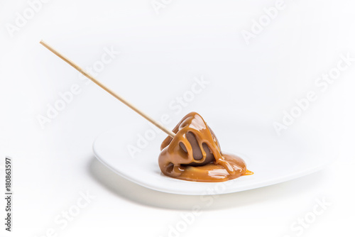 Hot chocolate stick covered in caramel on a plate white background
