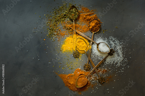 Bright spices in vintage spoons - saffron, salt, oregano, rosemary, red chili pepper on gray concrete background. Dark food photo.