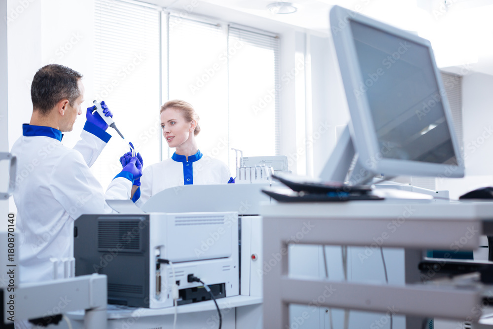 Analyzing process. Couple of young attractive laboratorians conducting analyses while standing behind the medical equipment and looking at each other Analyzing process. Couple of young attractive laboratorians conducting analyses while standing behind the medical equipment and looking at each other