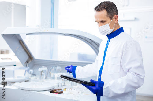 Cutting edge equipment. Attractive focused  male scientist reading instruction for innovative centrifuge machine  while holding tablet and standing in lab photo