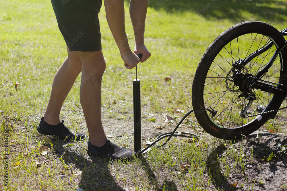Obraz premium Inflating the tire of a bicycle. Cyclist repairs bike in forest. Bicyclist pumping air into the wheel. Biker uses a bicycle pump. Pumping air into an empty wheel of bike.