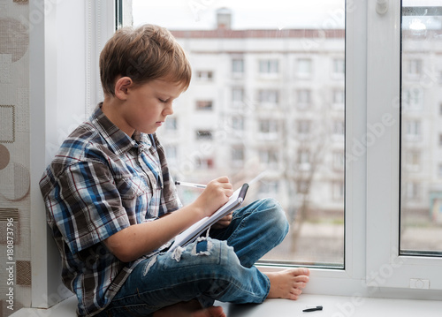 European boy writes poetry, sitting on the windowsill