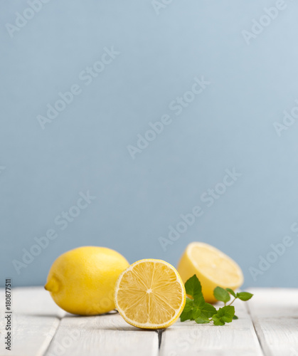 Ripe lemons and mint leaves on a white wooden table on a blue background..
