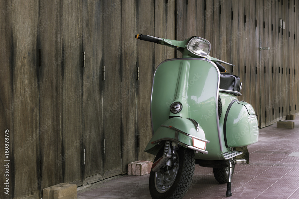 Green scooter against old house. wood wall mossy surface of building as background. Urban street in Thailand, Asia. Moped parked at moldy wood wall. Asian lifestyle and popular transport.