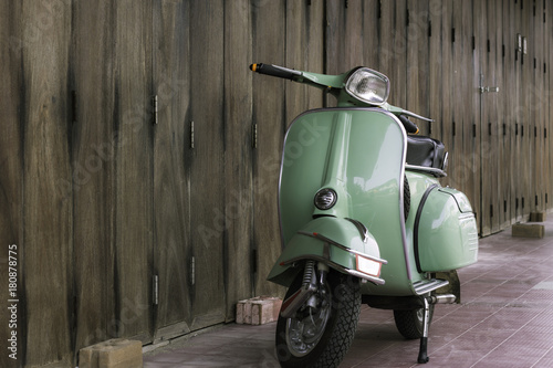 Green scooter against old house. wood wall mossy surface of building as background. Urban street in Thailand, Asia. Moped parked at moldy wood wall. Asian lifestyle and popular transport.